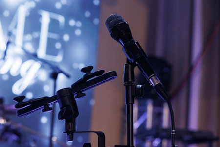 Microphone on stand on stage against a background of screen, close up. Mic technology. Voice, concert entertainment Speech broadcast equipment. Live pop, rock musical performance.の写真素材