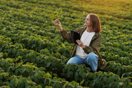 Smart farming soybean technology. Smiling female farmer with digital tablet uses for examine and check soya plants in field. Modern agribusiness of control of growth and development of sprouts.の写真素材