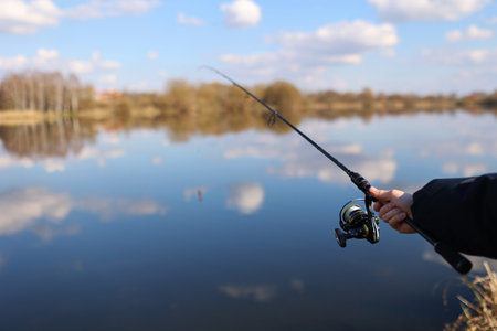 Man catching fish, pulling rod while fishing from lake or pond. Fisherman with rod, spinning reel on river bank. Fishing for pike, perch, carp on beach lake or pond. Wild nature, rural getawayの写真素材