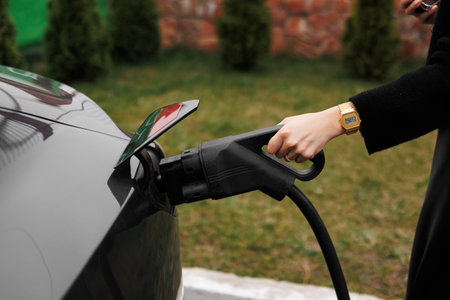 Unrecognisable woman inserting EV charger plug from public or home charging station for modern electric or hybrid car at special place for e-car. Concept eco-friendly sustainability energy carの写真素材