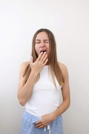 Caucasian young woman yawning and covering wide open mouth with hand isolated on white background. Girl looking sleepy and tired, exhausted for fatigue, lazy eyes in the morningの写真素材