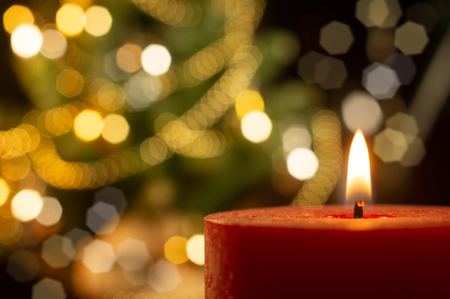 Lighted candle with the blurred Xmas tree with golden decoration on backgroundの写真素材