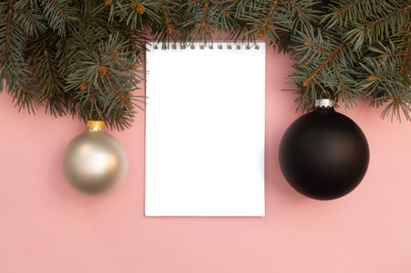 Black and pearl Christmas balls on the pink background and pine tree branches on top and note book...