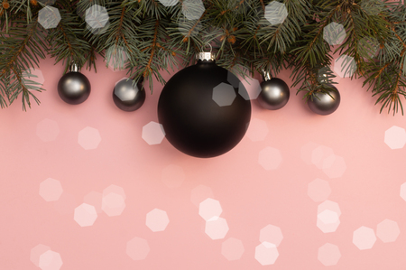 Black and pearl christmas balls on the top of pink background with pine tree branches and glows aroundの写真素材