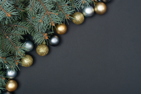 Christmas tree branches decorated with golden and silver baubles in top left corner of black background with copy spaceの写真素材