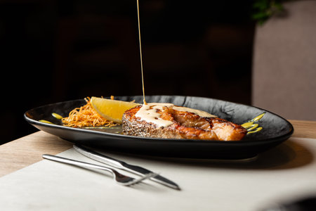 One piece of baked salmon steak grilled lemon and salt on a dark plate decorated with white sauce
