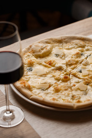 Four cheese pizza quattro formaggi with glass of wine on dark background.の写真素材