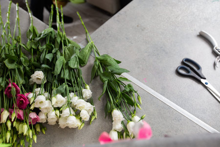 a female florist wrapping beautiful bouquet with paper at table, top view on the desktop. high...