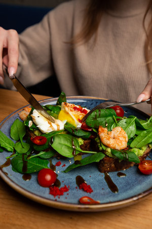 Buckwheat bread toasts with a poached egg, a sliced avocado, a shrimps, tomatoes and lettuce. Diet...