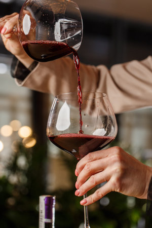 Male hand holds beautiful clear stemware for burgundy wine into which red wine is poured from...