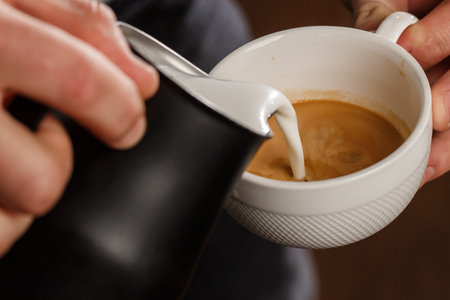 Professional barista pouring steamed milk into coffee glass cup making beautiful latte art Rosetta...
