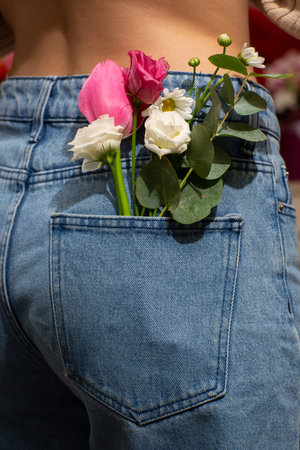 Woman with beautiful tender flowers in back pocket of jeans. Woman stabs back to camera. A tiny...