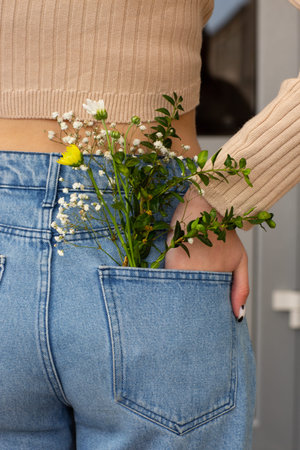 Woman with beautiful tender flowers in back pocket of jeans. Woman stabs back to camera. A tiny bouquet of field flowers in a back pocket of women's jeans.の写真素材