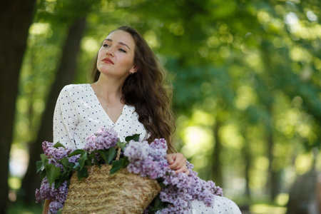 The girl in white dress holds in her hands a wicker basket with flowers. Basket with lilacs.