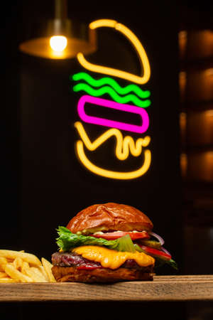Big cheeseburger with french fries isolated on background with neon burger sign . Hamburger with beef patty onion, tomato, lettuce pickles, melted cheddar, mustards, tomato jam, mayo.の写真素材