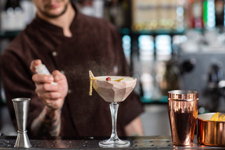 male bartender sprinkles on glass with cold cocktail decorated with dried pineappleの写真素材