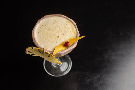 Glass with yellow lemon cocktail decorated with dried pineapple on the bar on a black background....