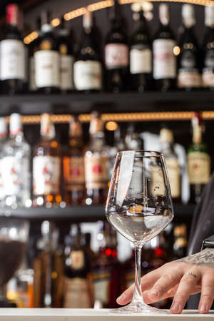 Low angle close up perspective of crystal clear wine glass with traditional round goblet shape and slim stem on counter top bar with blurryの写真素材