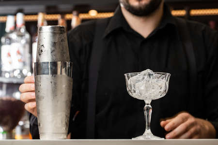 beautiful transparent glass with ice and steel cup stand on the bar counter. In the background, the bartender rubsの写真素材