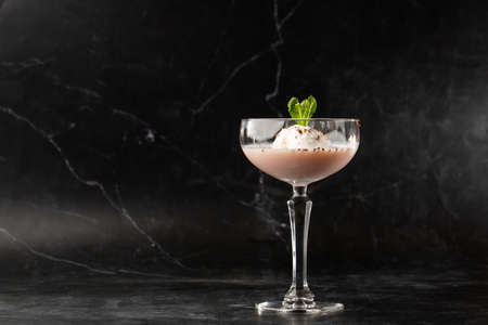 Glass of ice cold cocktail served in a glass, decorated with mint leaf placed on a blackの写真素材