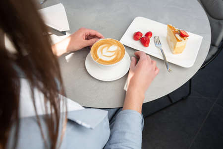Girl enjoy classic cheesecake with fresh strawberry with cup of coffee on white table. close-up view. Tasty breakfast. Piece of cake on plate, white cup on white marble background.の写真素材