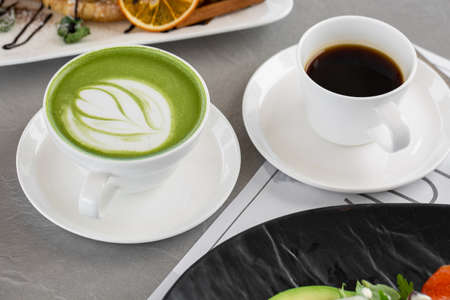 Cup of matcha latte and coffee. High quality photo. Matcha, green tea latte in a cup and croissant. gray background. close up. top viewの写真素材