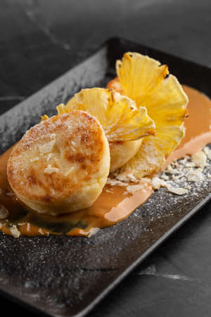 Cottage cheese pancakes, Syrniki or Cheesecakes with dried pineapple and caramel isolated on black marble background. homemade food. Tasty breakfast. selective focus.の写真素材