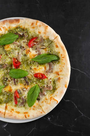 Delicious hot homemade pizza on black marble table. Pizza - Fresh homemade pizza with meat, cheese, tomato sauce, tomatoes, pumpkin seeds and basilの写真素材