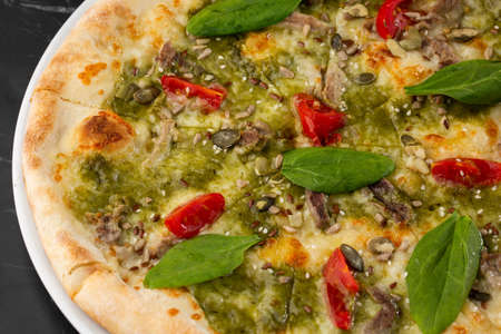Delicious hot homemade pizza on black marble table. Pizza - Fresh homemade pizza with meat, cheese, tomato sauce, tomatoes, pumpkin seeds and basilの写真素材