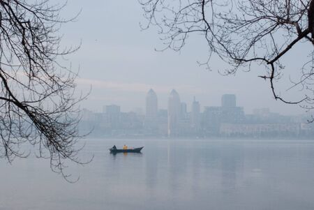 Fishing boat on the Dnieper river in Ukraine against the background of Dnipro city in the dawn fog. Dnipro is Ukraine's fourth-largest city, with about one million inhabitants.の写真素材