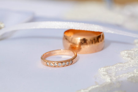 couple of gold wedding diamond rings on white wedding pillow