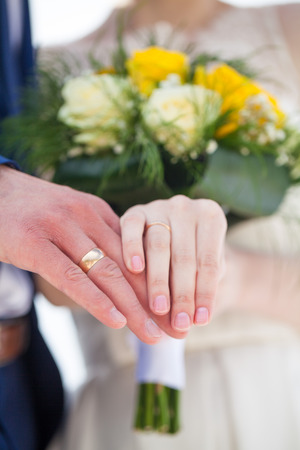 Wedding couple hands on flowers with golden ringsの写真素材
