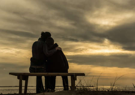 Mother and son sitting on the beach and watching sunsetの写真素材
