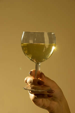 Womans hand holding a glass of white wine on a beige backgroundの写真素材