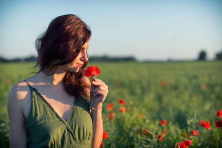 Young woman smelling poppy flower in green dressの写真素材