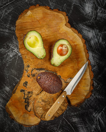 still life with whole and halved avocado on wooden plateの写真素材