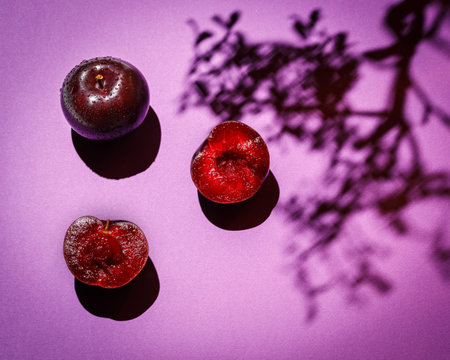 still life with plums on color background and tree shadow