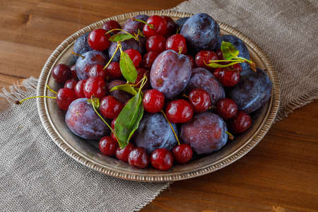 fresh plums and cherries on a plate on wooden tableの写真素材