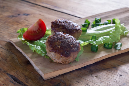 Two meatballs and vegetables on a wooden board. close up
