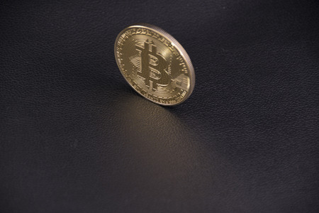 gold coin bitcoin stands upright on black leather casts a Golden glareの写真素材