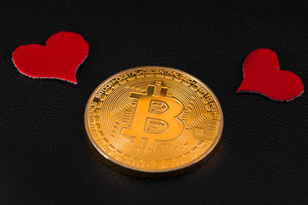 two little red hearts over a bitcoin gold coin on black leather closeup