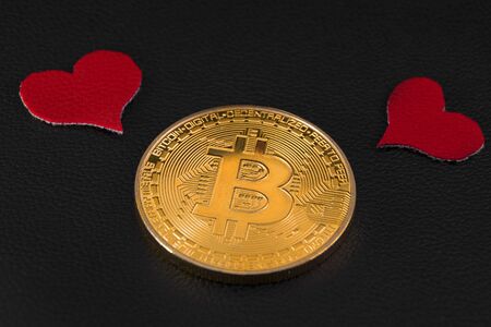 two little red hearts over a bitcoin gold coin on black leather closeupの写真素材