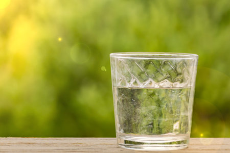 glass of water on a wooden table background of green bokeh
