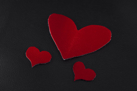 two small and large red hearts on black skin close-up