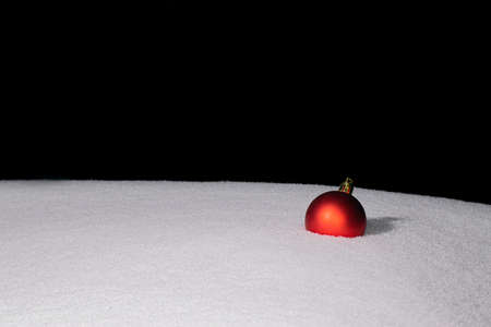 one red Christmas ball is lying on the snowの写真素材