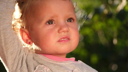 The sun illuminates the face of a small child, she looks up. Surprised look of a little girl.