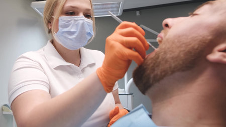 Female dentist treats young mans teeth, dentists office. Dental treatment concept.