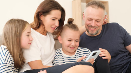 Happy family looking at smartphone, they are sitting on the couch and smiling.