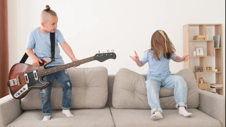 Little boy playing electric guitar, children having fun at home on the couch. Brother and sisterの写真素材