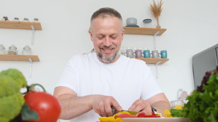 Smiling chef slices fresh vegetables sitting at the table in the kitchen. The chef prepares a salad